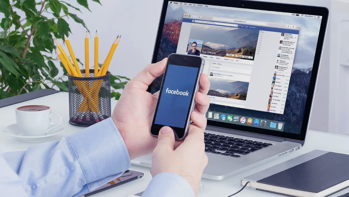 Man opens Facebook on his smartphone notebook on the Background
